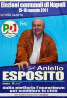 il candidato esposito, del pd, in una strana postura obliqua, si regge con una mano al bordo della scritta